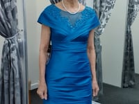 Elegant teal blue taffeta dress with ruched details and shimmering embellishments, showcased on a female model in a dressing room. Elegant teal blue taffeta dress with ruched details and shimmering embellishments, showcased on a female model in a dressing room.