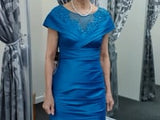 Elegant teal blue taffeta dress with ruched details and shimmering embellishments, showcased on a female model in a dressing room. Elegant teal blue taffeta dress with ruched details and shimmering embellishments, showcased on a female model in a dressing room.