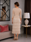Back view of a champagne beaded fringe mother of the bride dress featuring a fitted bodice, three-quarter sleeves and tiered fringe skirt, modelled by a brunette size 12–14 woman in a sophisticated indoor setting.