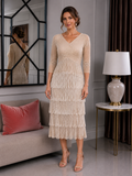 Champagne beaded fringe mother of the bride dress with V-neckline and three-quarter sleeves, shown on a brunette size 12–14 model in an elegant indoor boutique setting.