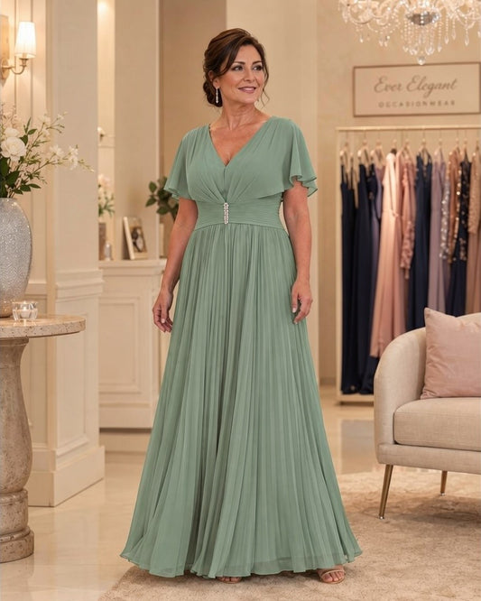 Aqua teal pleated full-length gown with flutter sleeves and jewelled waist, front view on a mature brunette model.
