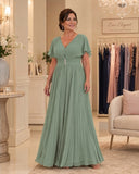 Aqua teal pleated full-length gown with flutter sleeves and jewelled waist, front view on a mature brunette model.