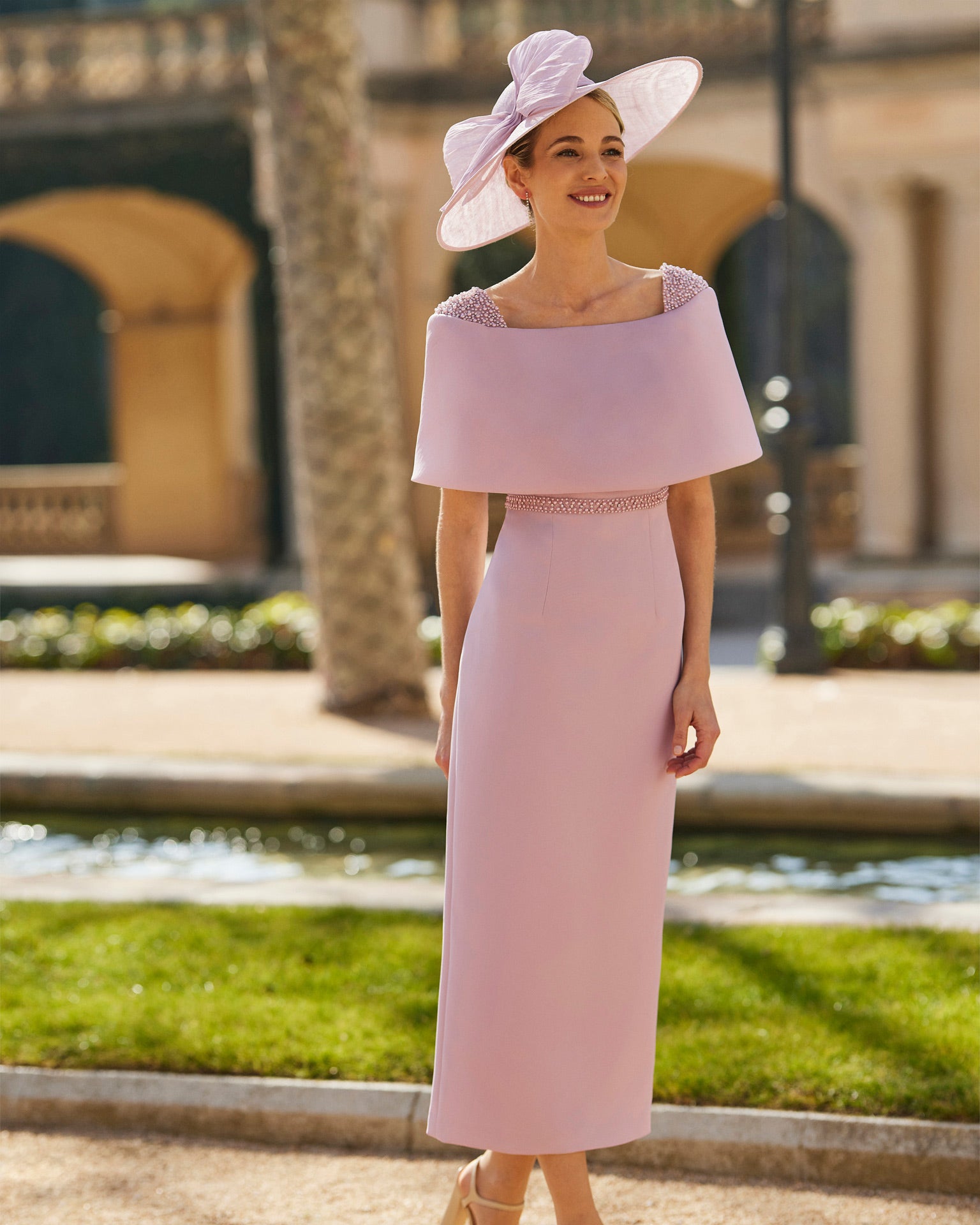 Stylish pink midi dress with off-the-shoulder design and oversized collar, accessorized with a wide-brimmed hat, showcased in an elegant outdoor setting.