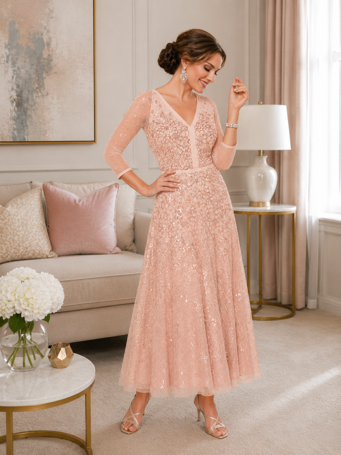 Blush pink embellished tea-length occasion dress with sheer three-quarter sleeves, fitted bodice and flowing A-line skirt, styled for mother of the bride or mother of the groom in an elegant indoor boutique setting.