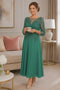 Emerald green tea-length mother of the bride dress with intricate beaded bodice, illusion neckline, three-quarter sleeves, and flowing crepe skirt on a mature brunette model in an elegant indoor boutique setting.