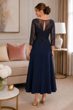 Back view of navy tea-length mother of the bride dress featuring a sheer illusion keyhole back, detailed beaded lace overlay, three-quarter sleeves, and a structured crepe A-line skirt on a mature brunette model in a luxury indoor boutique setting.