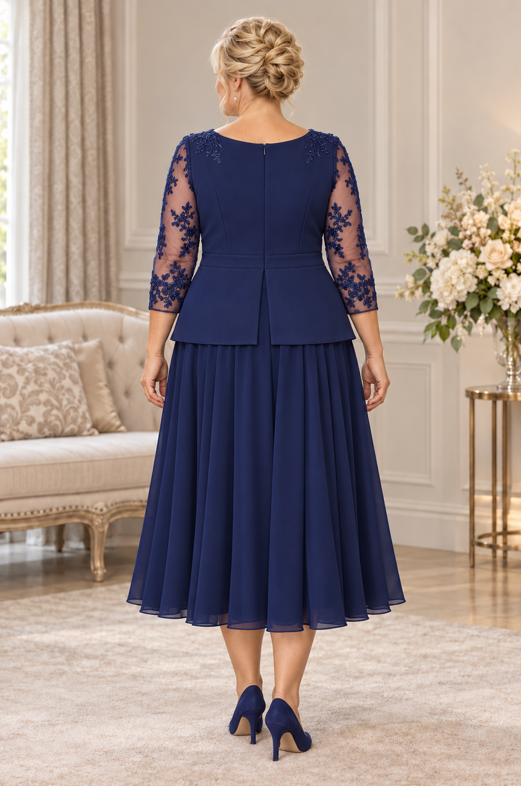 Back view of navy plus size dress featuring lace sleeves, shoulder appliqué, centre-back peplum split and flowing chiffon skirt.