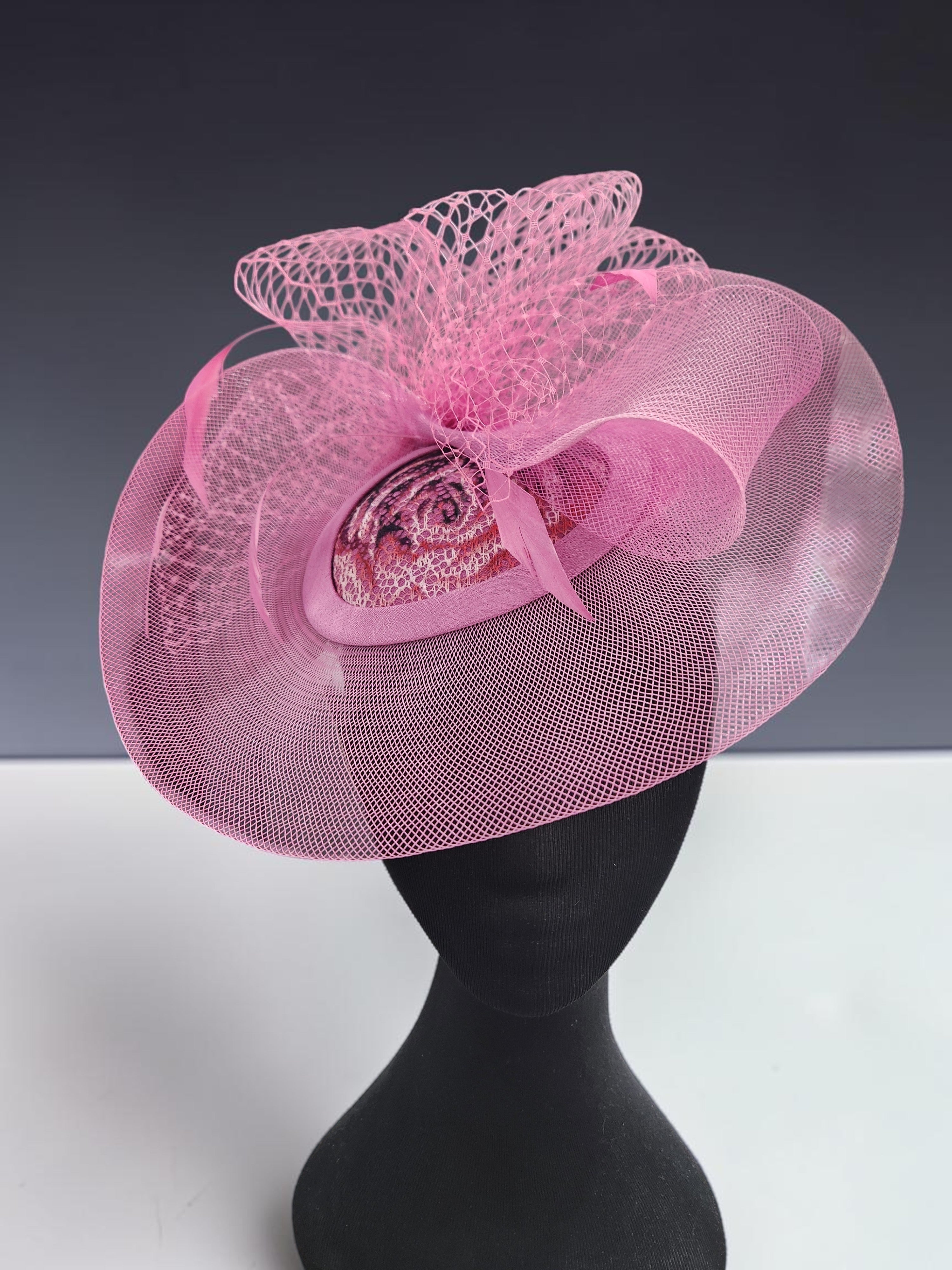 Close-up of pink fabric occasion fascinator with patterned centre and mesh loops 