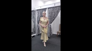 A video  showcasing a cream gold off-the-shoulder mother of the bride dress with draped front detail, fitted silhouette and elegant movement in an indoor boutique setting.