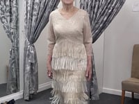 Video of a champagne beaded fringe mother of the bride dress showcasing the front, side and back views, highlighting intricate beadwork, tiered fringe detailing and elegant movement on a brunette size 12–14 model.